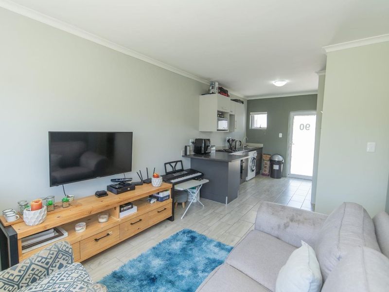 Open plan living area featuring a compact kitchen with built-in cabinetry and tiled flooring, leading to an exterior entrance door.