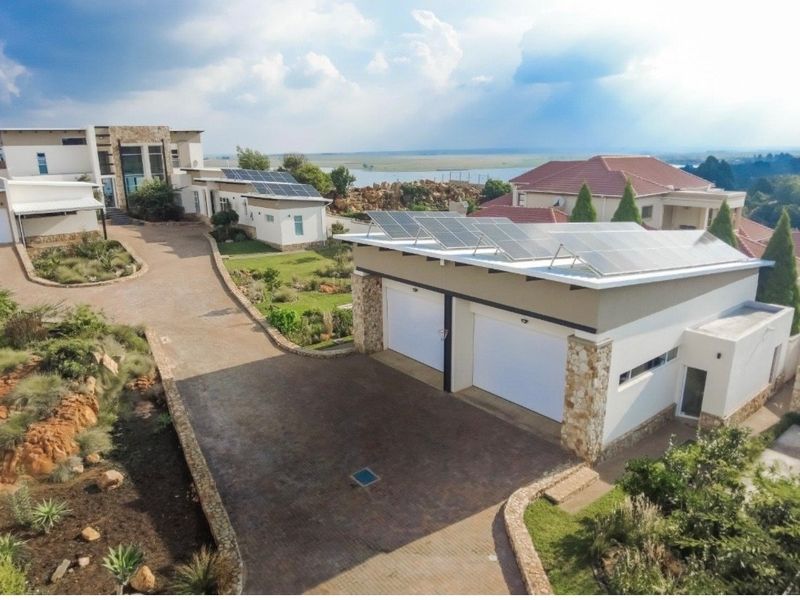 Aerial view of a modern residential property featuring a double garage with solar panels, a paved driveway, and landscaped garden areas.