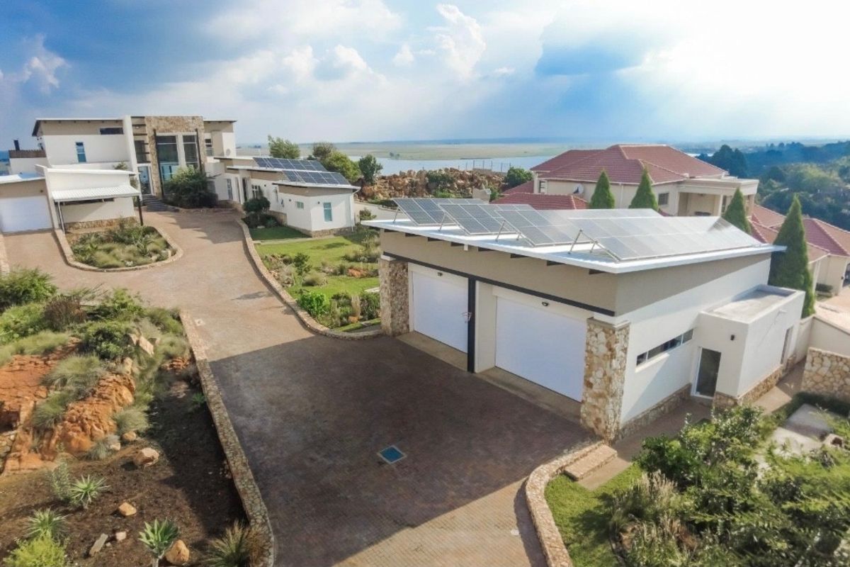 Aerial view of a modern residential property featuring a double garage with solar panels, a paved driveway, and landscaped garden areas.