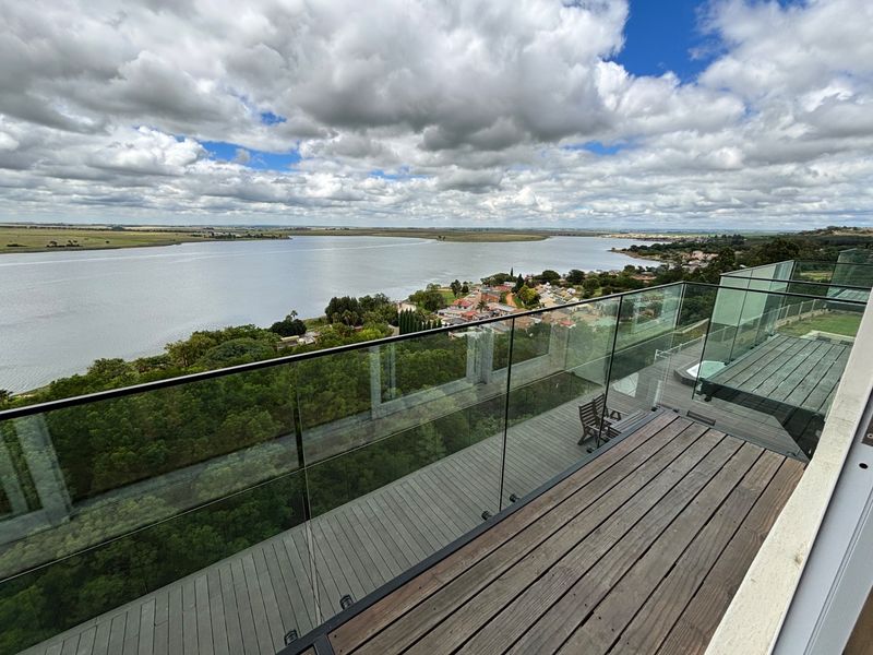 Spacious elevated timber balcony featuring a frameless glass balustrade and built-in spa, offering expansive panoramic views of the lake and surrounding landscape.