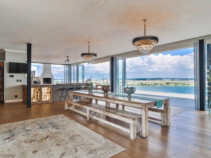 Spacious open-plan living area featuring a built-in bar, fireplace, and expansive stacking glass doors opening to a scenic waterfront view.