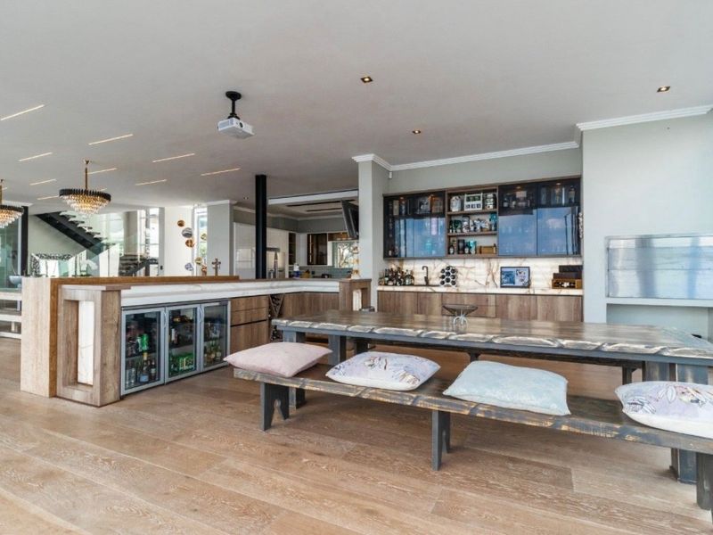 Spacious open-plan living area featuring a modern built-in bar with integrated beverage fridges, stone countertops, and high-quality hardwood flooring throughout.
