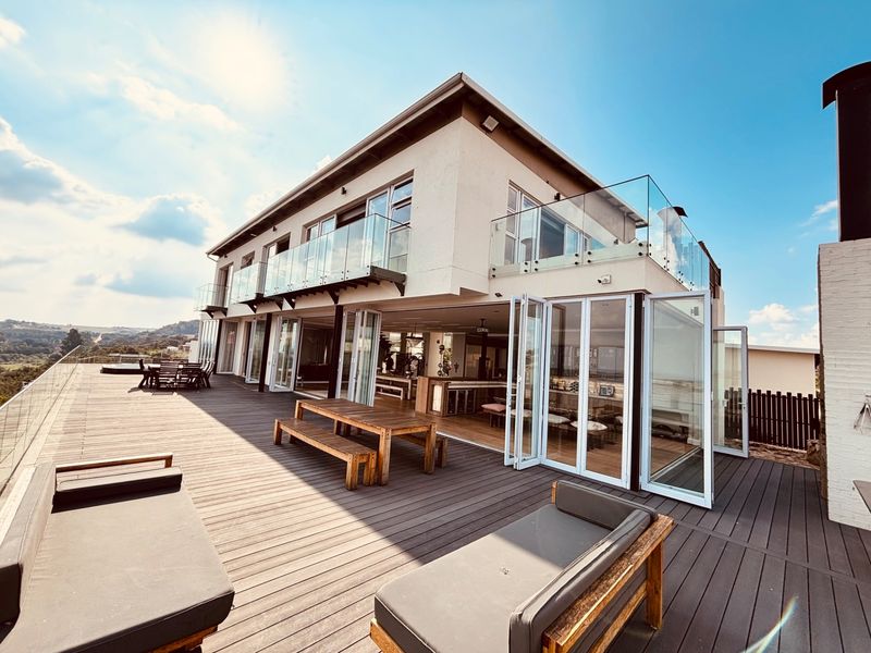 Expansive elevated timber deck featuring glass balustrades and seamless indoor-outdoor flow through large bi-fold doors, offering a modern entertainment space.