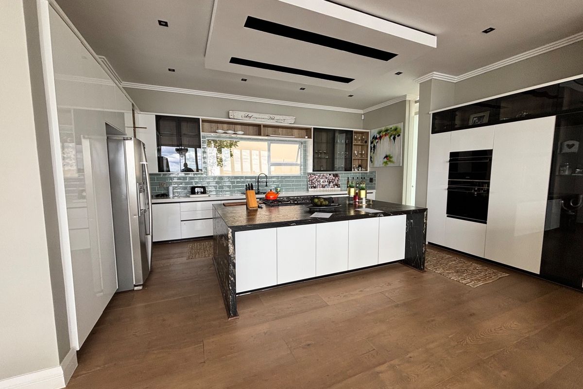 Modern kitchen featuring a large central island with stone countertops, high-end built-in appliances, sleek cabinetry, and a stylish drop ceiling with recessed lighting.