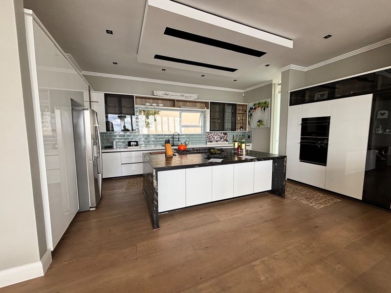 Modern kitchen featuring a large central island with stone countertops, high-end built-in appliances, sleek cabinetry, and a stylish drop ceiling with recessed lighting.