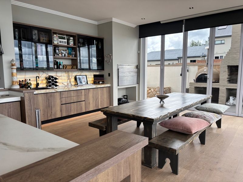 Modern open-plan living and entertainment area featuring high-end cabinetry, stone countertops, and seamless indoor-outdoor flow through large bi-fold doors to the patio.
