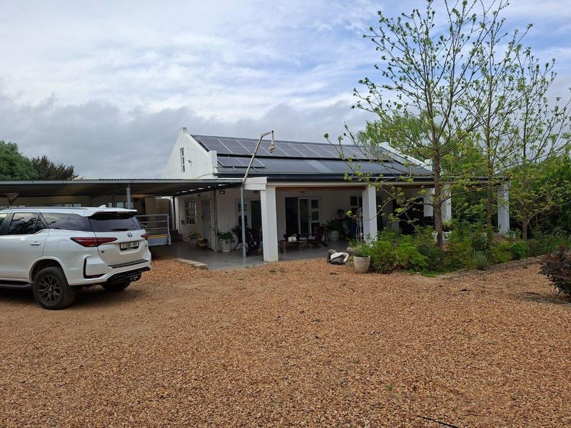 Front view of a farm-style residence featuring a covered patio, gravel driveway, and roof-mounted solar panels.