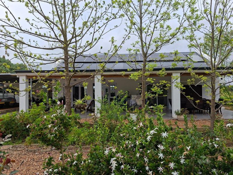 A covered patio area featuring concrete pillars and a roof equipped with solar panels, overlooking a landscaped garden.