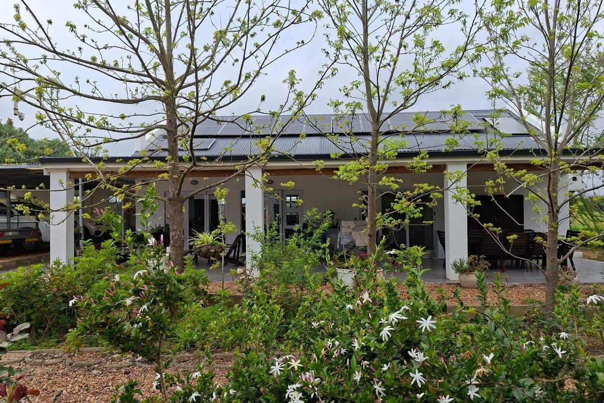 A covered patio area featuring concrete pillars and a roof equipped with solar panels, overlooking a landscaped garden.