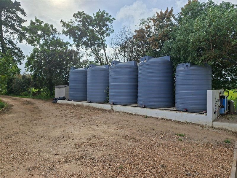 A row of five large grey water storage tanks mounted on a raised concrete plinth with an integrated water filtration system.