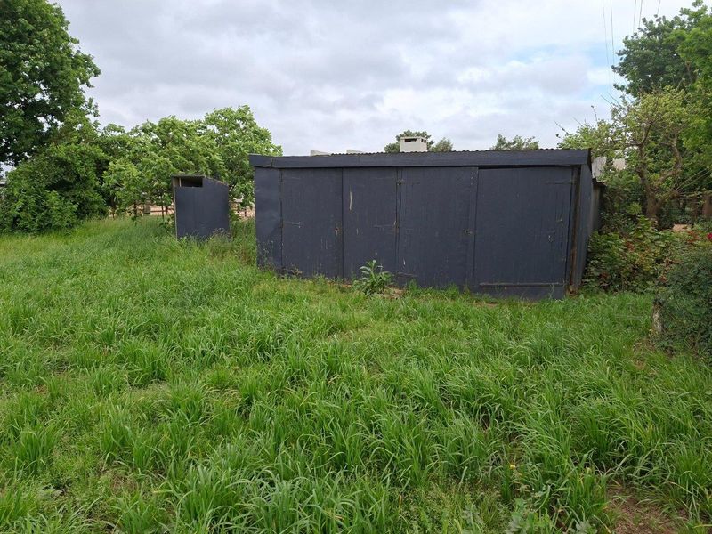 A detached utility storage structure located on a farm property, featuring a chimney stack and requiring exterior maintenance.