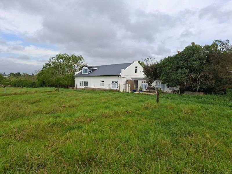 A view of the rear elevation of a farmhouse featuring a pitched roof, white exterior walls, and a patio area overlooking a grassy field.