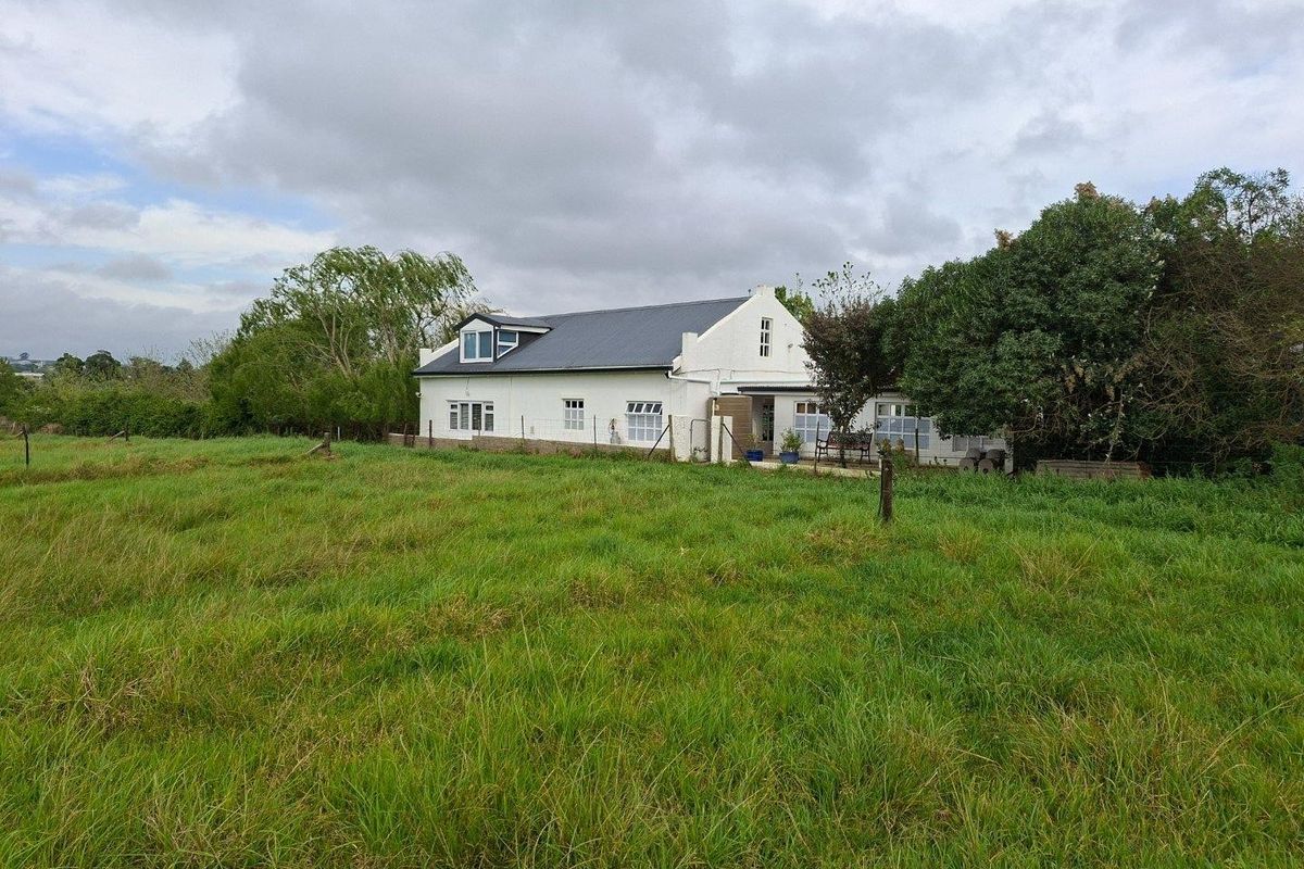 A view of the rear elevation of a farmhouse featuring a pitched roof, white exterior walls, and a patio area overlooking a grassy field.
