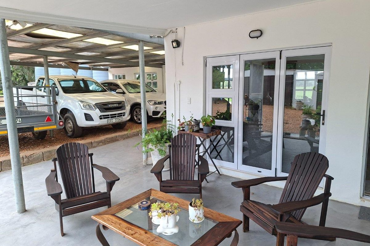 A covered patio area featuring concrete flooring and glass sliding doors, providing a functional outdoor space adjacent to a covered parking area.