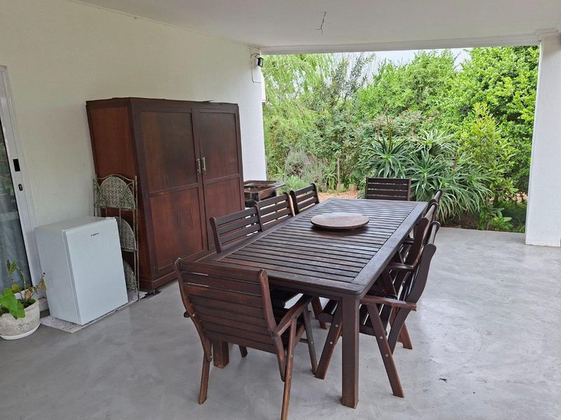 A covered outdoor patio area featuring concrete flooring, providing a functional space for outdoor dining and relaxation overlooking the garden.