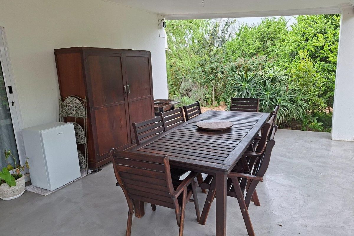 A covered outdoor patio area featuring concrete flooring, providing a functional space for outdoor dining and relaxation overlooking the garden.