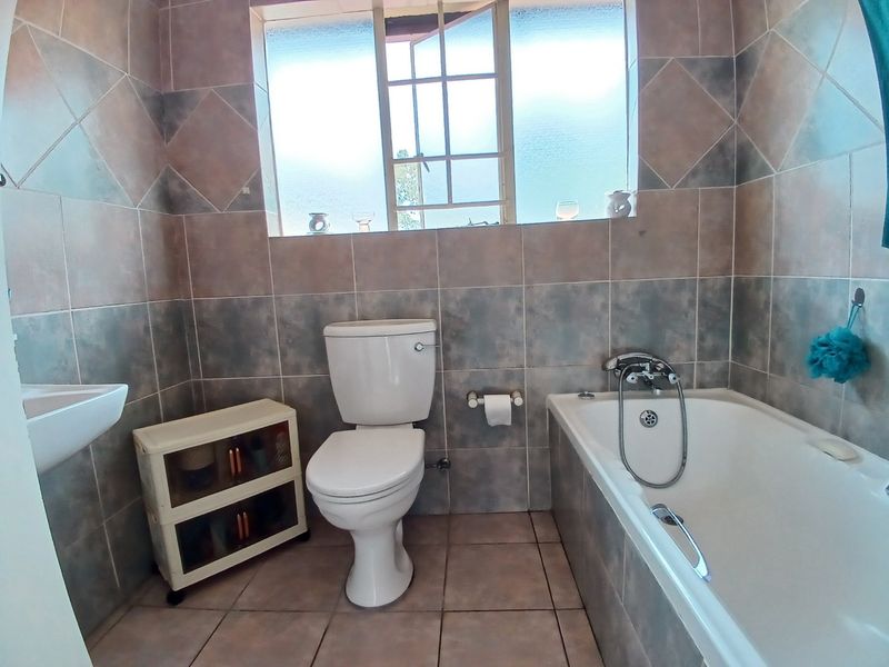 A functional bathroom featuring a bathtub, toilet, and hand basin with full-height wall tiling and a window for natural light.