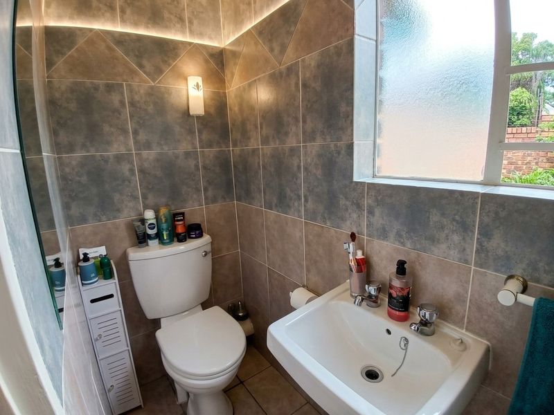 A compact bathroom featuring modern two-tone ceramic wall tiling, a white washbasin, a toilet, and a frosted glass window for natural light.