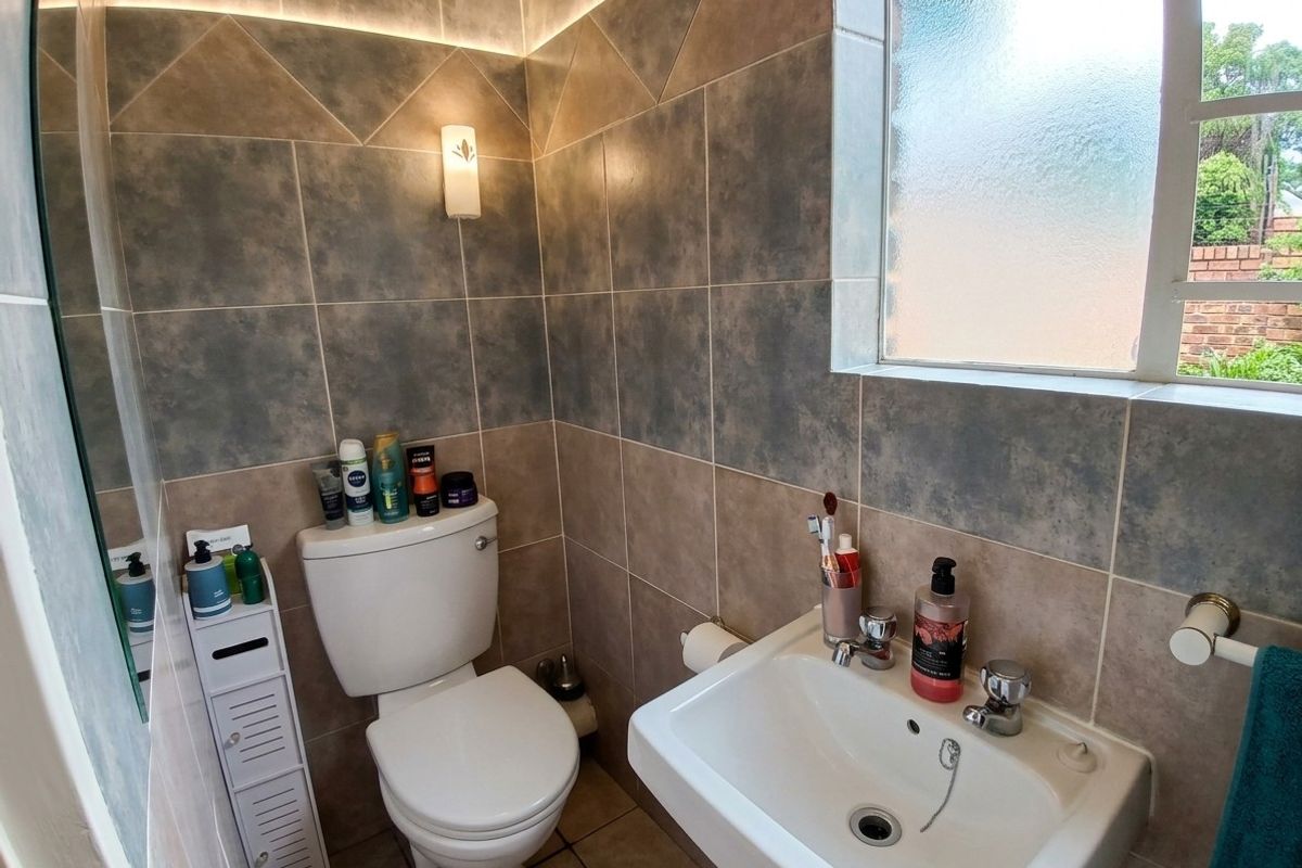 A compact bathroom featuring modern two-tone ceramic wall tiling, a white washbasin, a toilet, and a frosted glass window for natural light.