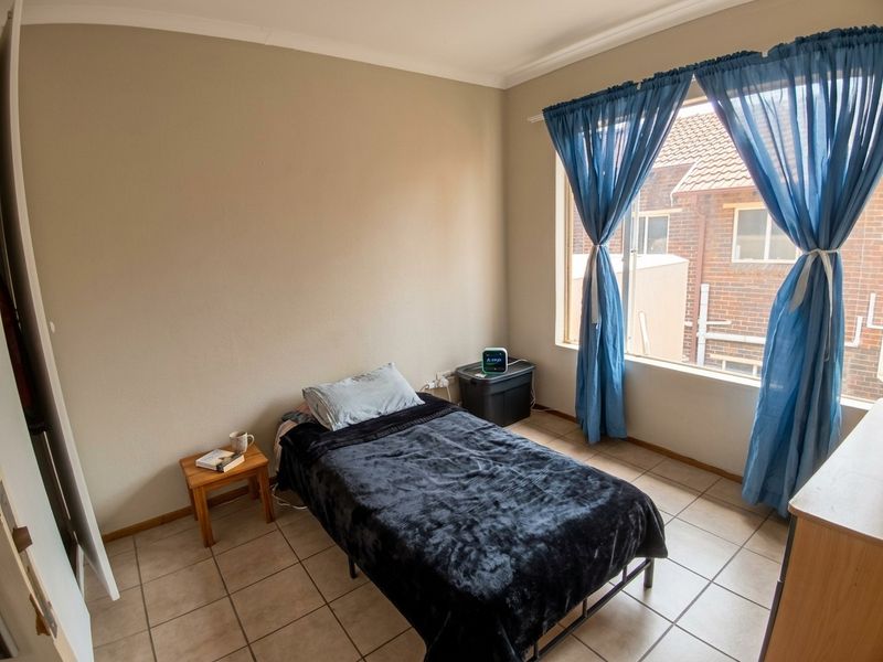 A functional bedroom featuring tiled flooring and a large window that provides natural light and a view of the neighboring property.