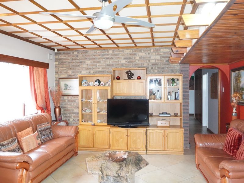 A living room featuring a distinctive coffered ceiling, exposed brick accent wall, tiled flooring, and an arched entryway leading to other areas of the home.