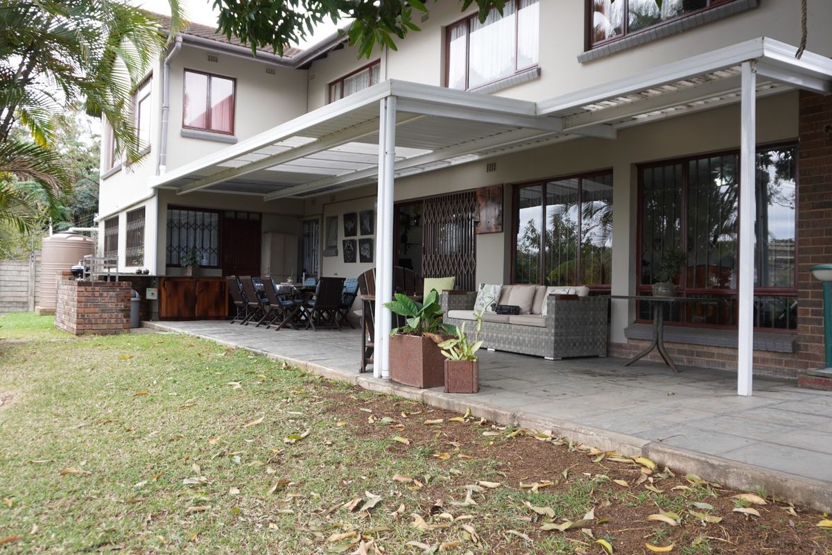 Spacious rear patio featuring paved flooring and a covered structure, overlooking the garden area with integrated brick masonry and security features.