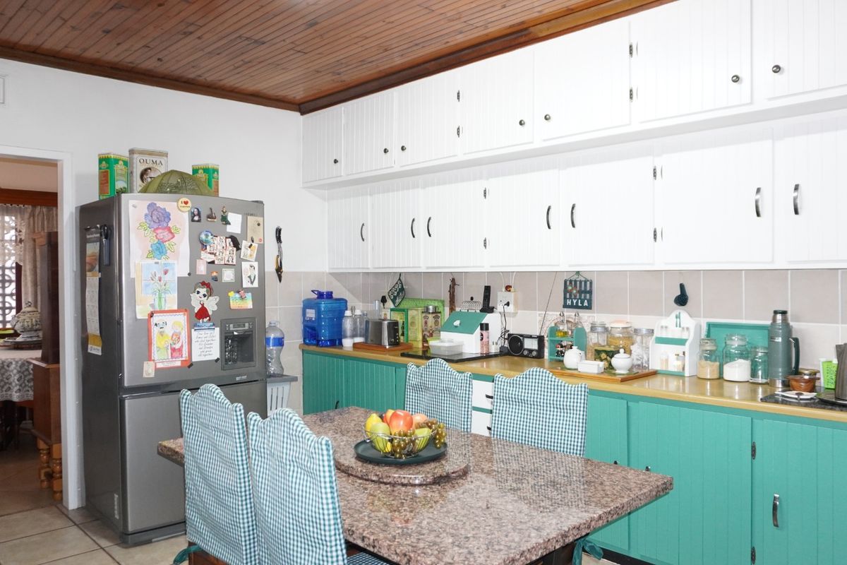 A functional kitchen featuring white upper cabinetry, green lower cabinets, granite countertops, a tiled backsplash, and a distinctive timber-paneled ceiling.