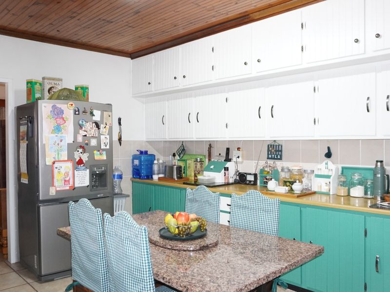 A functional kitchen featuring white upper cabinetry, green lower cabinets, granite countertops, a tiled backsplash, and a distinctive timber-paneled ceiling.