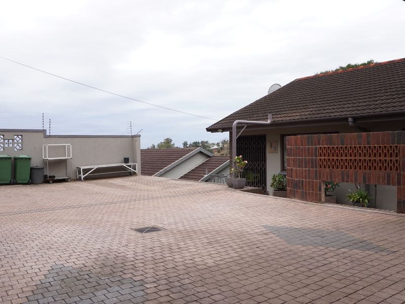 A paved front driveway area featuring a brick boundary wall, security gate, and tiled roof structure with electric fencing.