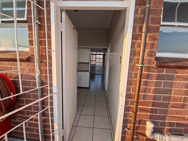Exterior view of a building entrance featuring brick facade, tiled flooring, and access to an interior hallway with built-in cabinetry.