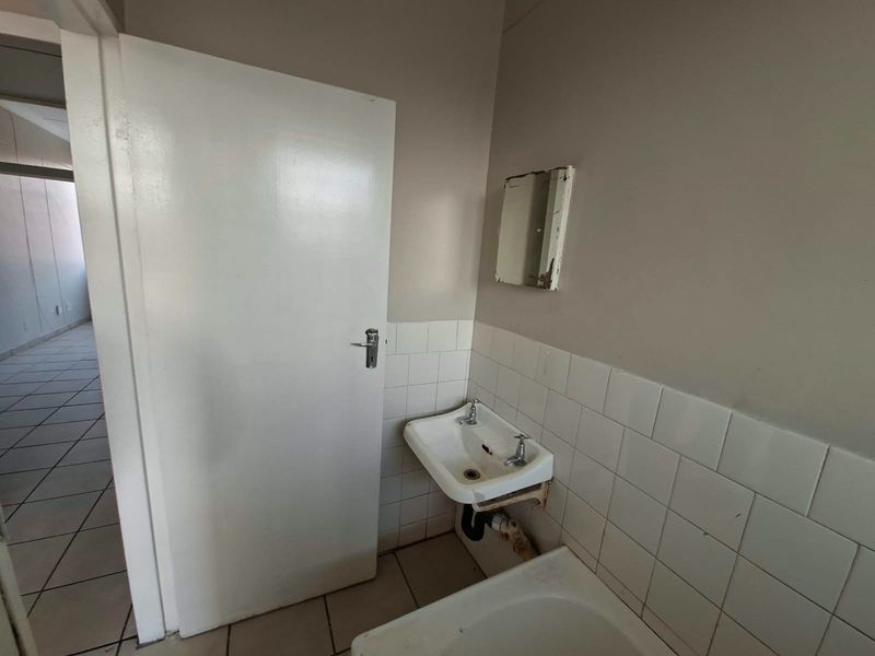 A small, functional bathroom space featuring a wall-mounted basin with tiled splashback and neutral floor tiles, requiring minor cosmetic updates.