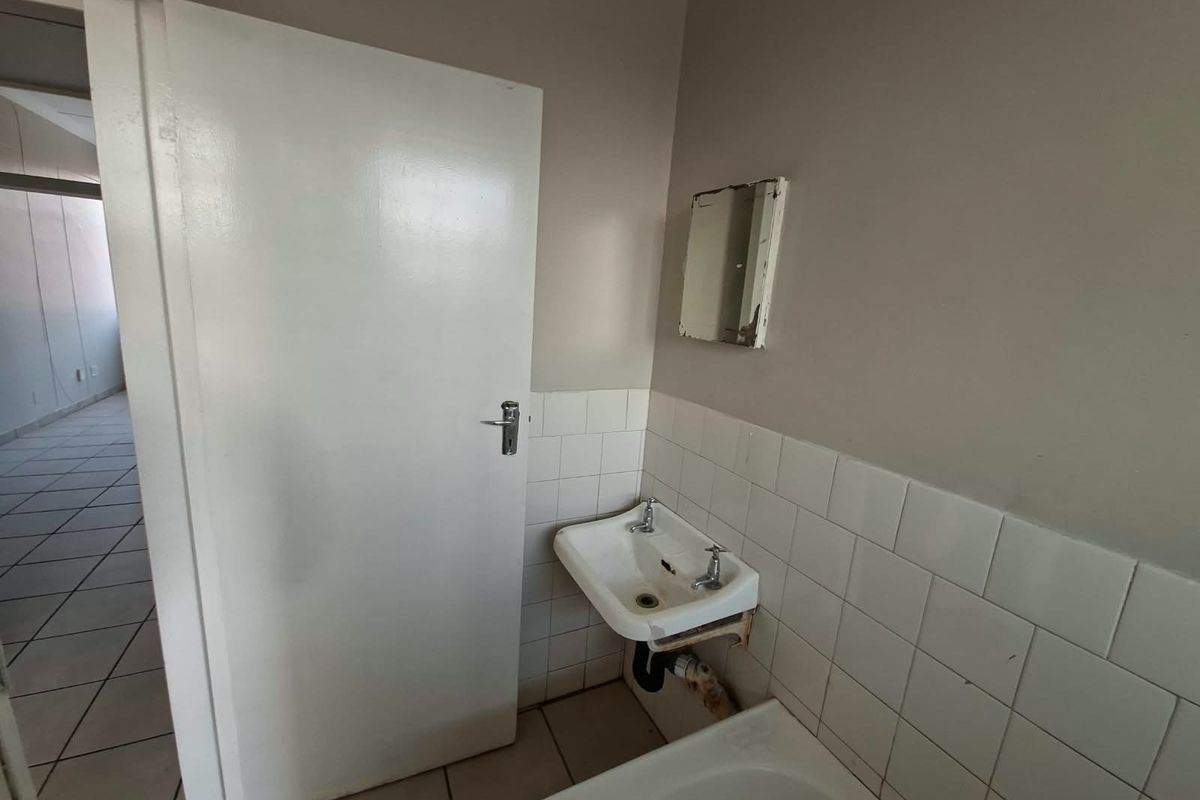 A small, functional bathroom space featuring a wall-mounted basin with tiled splashback and neutral floor tiles, requiring minor cosmetic updates.