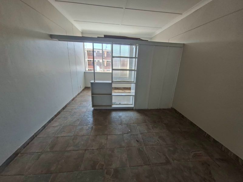 An empty bedroom featuring tiled flooring, a built-in shelving partition, and coved ceilings, offering a blank canvas for renovation or interior design updates.