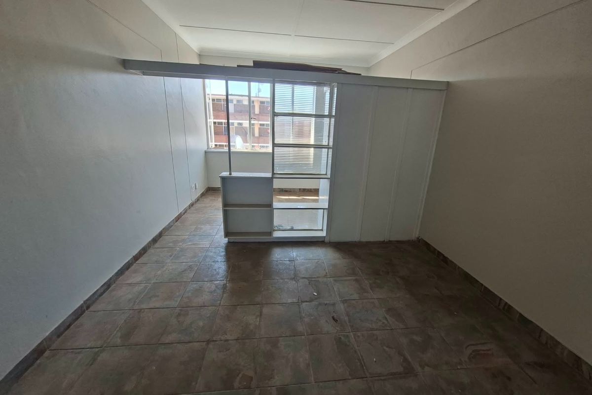 An empty bedroom featuring tiled flooring, a built-in shelving partition, and coved ceilings, offering a blank canvas for renovation or interior design updates.
