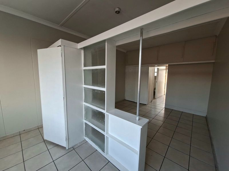 An empty bedroom featuring built-in cupboards, overhead storage, and a decorative ribbed glass room divider with ceramic tiled flooring.