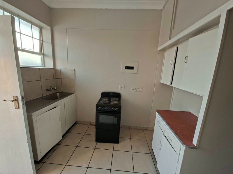 A functional, compact kitchen featuring tiled flooring, built-in cabinetry, a stainless steel sink, and a freestanding stove, offering a blank canvas for renovation.