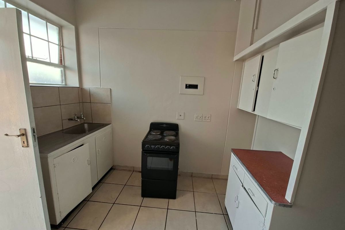 A functional, compact kitchen featuring tiled flooring, built-in cabinetry, a stainless steel sink, and a freestanding stove, offering a blank canvas for renovation.