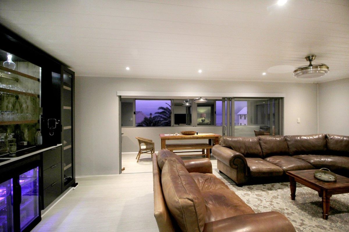 Spacious living area featuring recessed lighting, a ceiling fan, and a built-in bar with integrated wine cooler, opening onto an outdoor patio.
