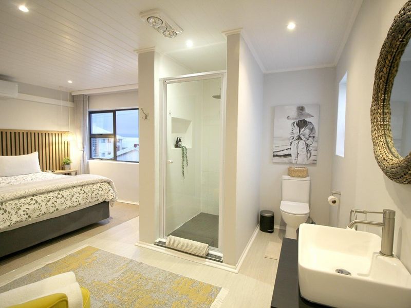 A modern bedroom featuring an integrated open-plan ensuite with a glass-enclosed shower, vanity, and toilet, complemented by contemporary finishes and recessed lighting.