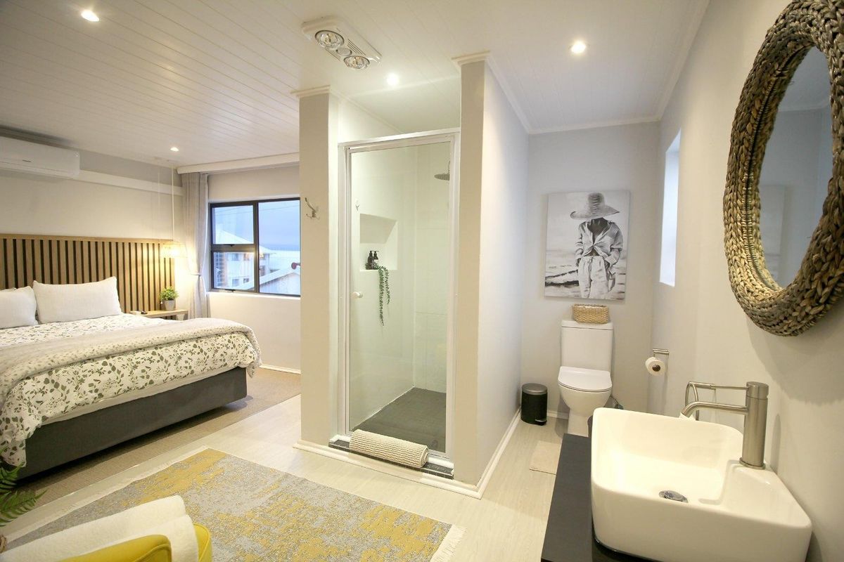 A modern bedroom featuring an integrated open-plan ensuite with a glass-enclosed shower, vanity, and toilet, complemented by contemporary finishes and recessed lighting.