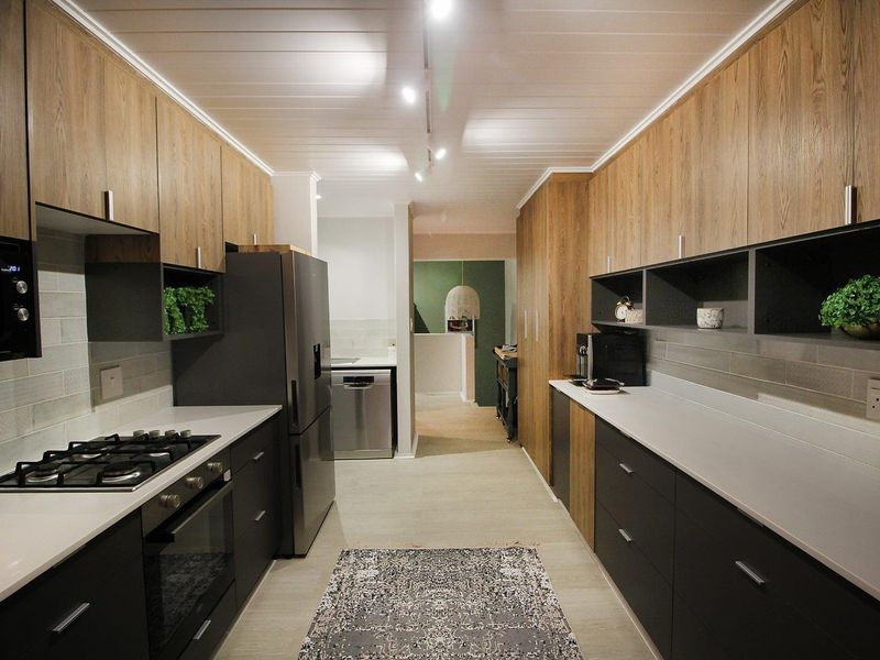 Modern galley-style kitchen featuring sleek wood-tone and dark cabinetry, stone countertops, subway tile backsplash, and integrated gas cooking appliances.