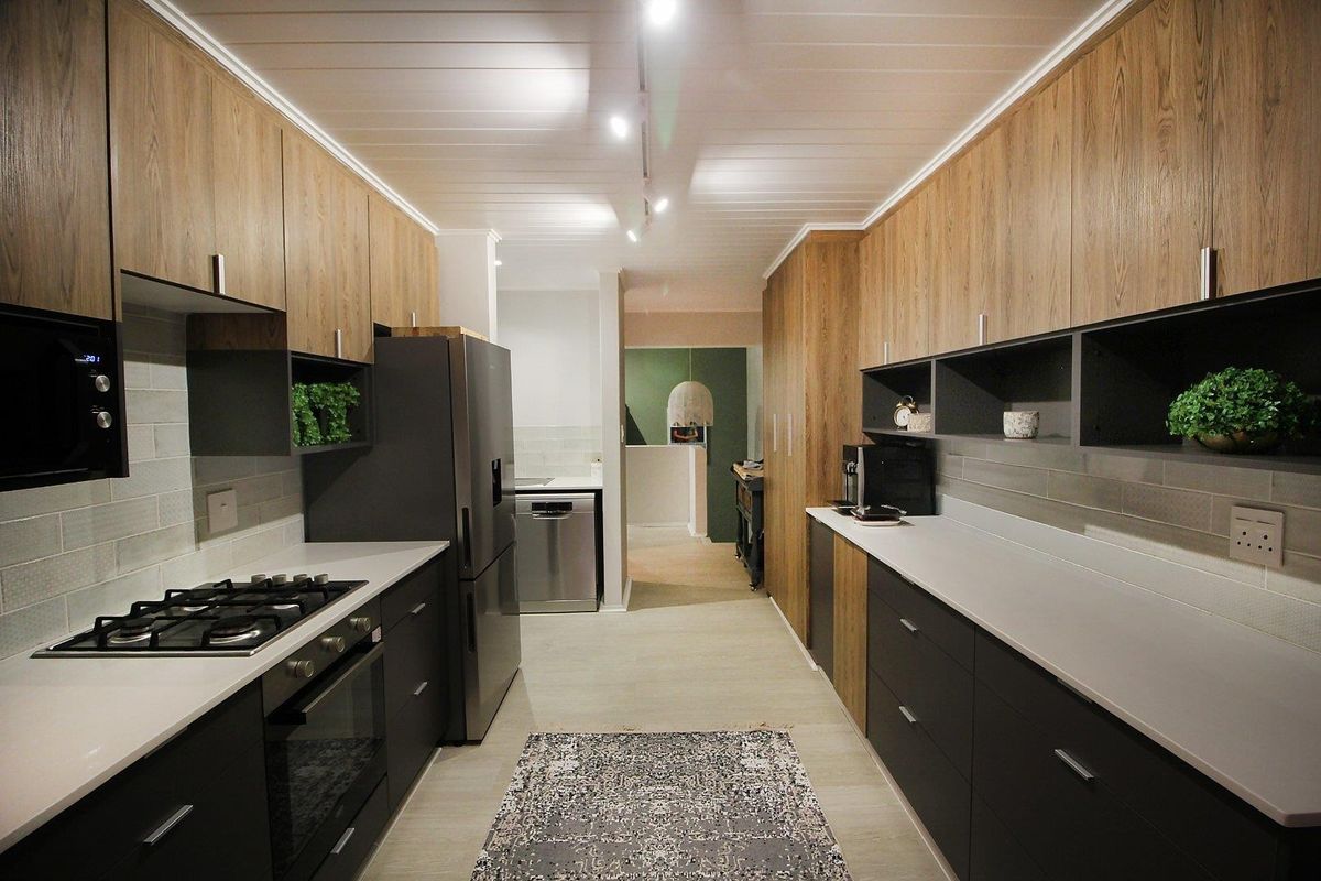 Modern galley-style kitchen featuring sleek wood-tone and dark cabinetry, stone countertops, subway tile backsplash, and integrated gas cooking appliances.