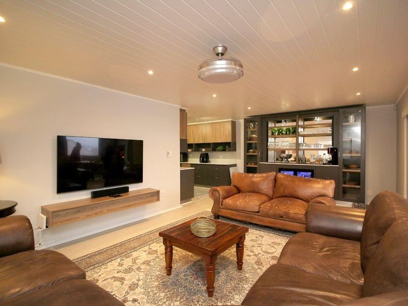 Spacious open-plan living area featuring a modern built-in bar, floating media console, recessed lighting, and a stylish tongue and groove ceiling.