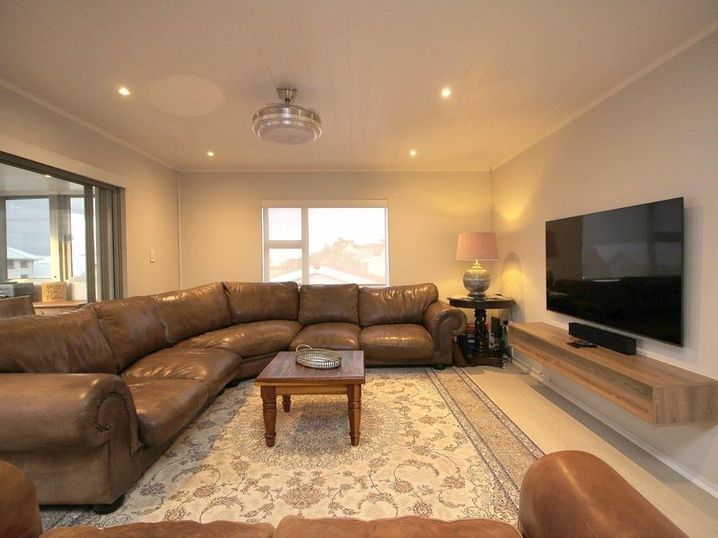 A well-maintained living room featuring recessed lighting, a ceiling fan, and a modern floating media console with access to an outdoor area.