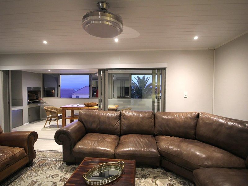 Spacious open-plan living area featuring recessed lighting, a ceiling fan, and seamless flow to an adjacent covered patio with a built-in braai.