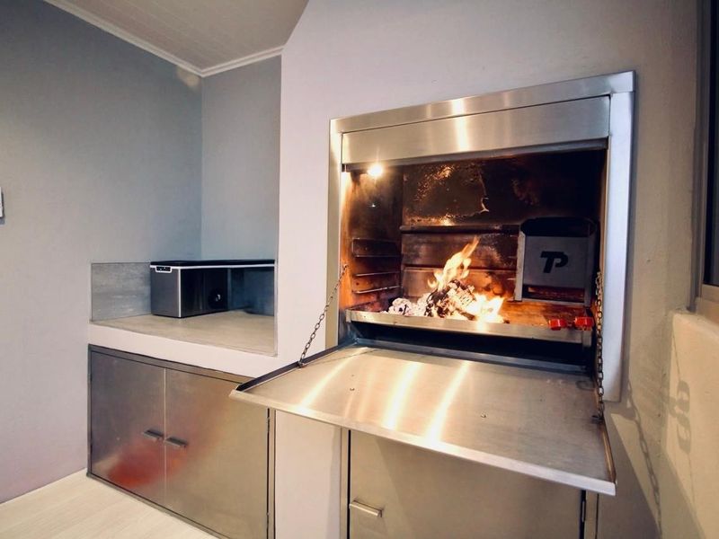 A clean, modern indoor entertainment area featuring a built-in stainless steel braai with integrated cabinetry and concrete prep surfaces.