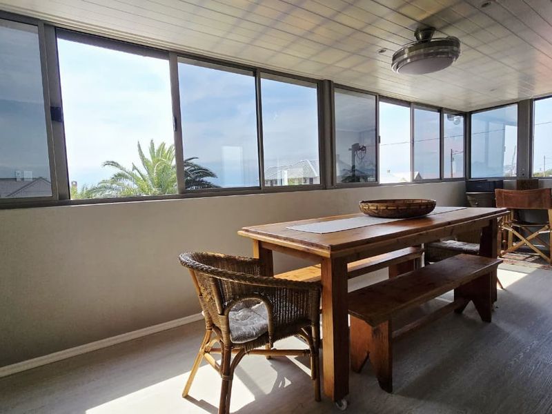A bright, enclosed patio area featuring large sliding windows, laminate flooring, and a ceiling fan, offering a versatile space for dining or relaxation.