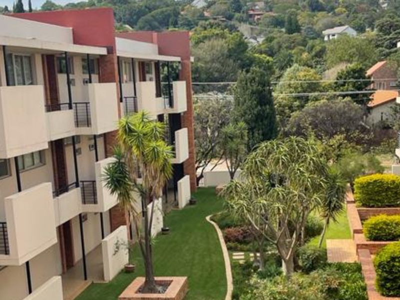 View of an apartment complex exterior featuring brick facades, private balconies, and a well-maintained communal garden area.