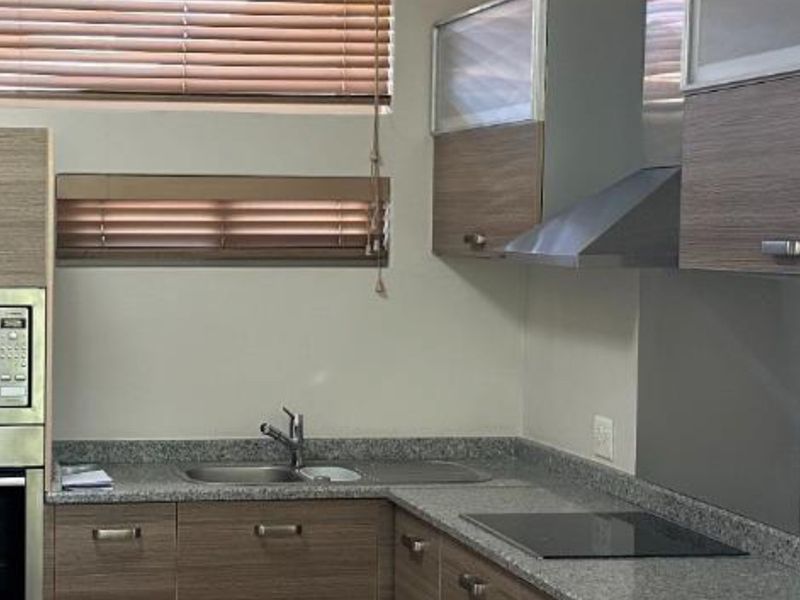 Modern kitchen featuring granite countertops, built-in oven, microwave, extractor fan, and sleek wood-veneer cabinetry with integrated sink and hob.