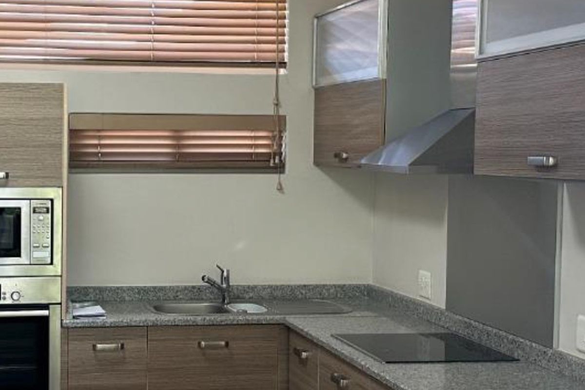 Modern kitchen featuring granite countertops, built-in oven, microwave, extractor fan, and sleek wood-veneer cabinetry with integrated sink and hob.